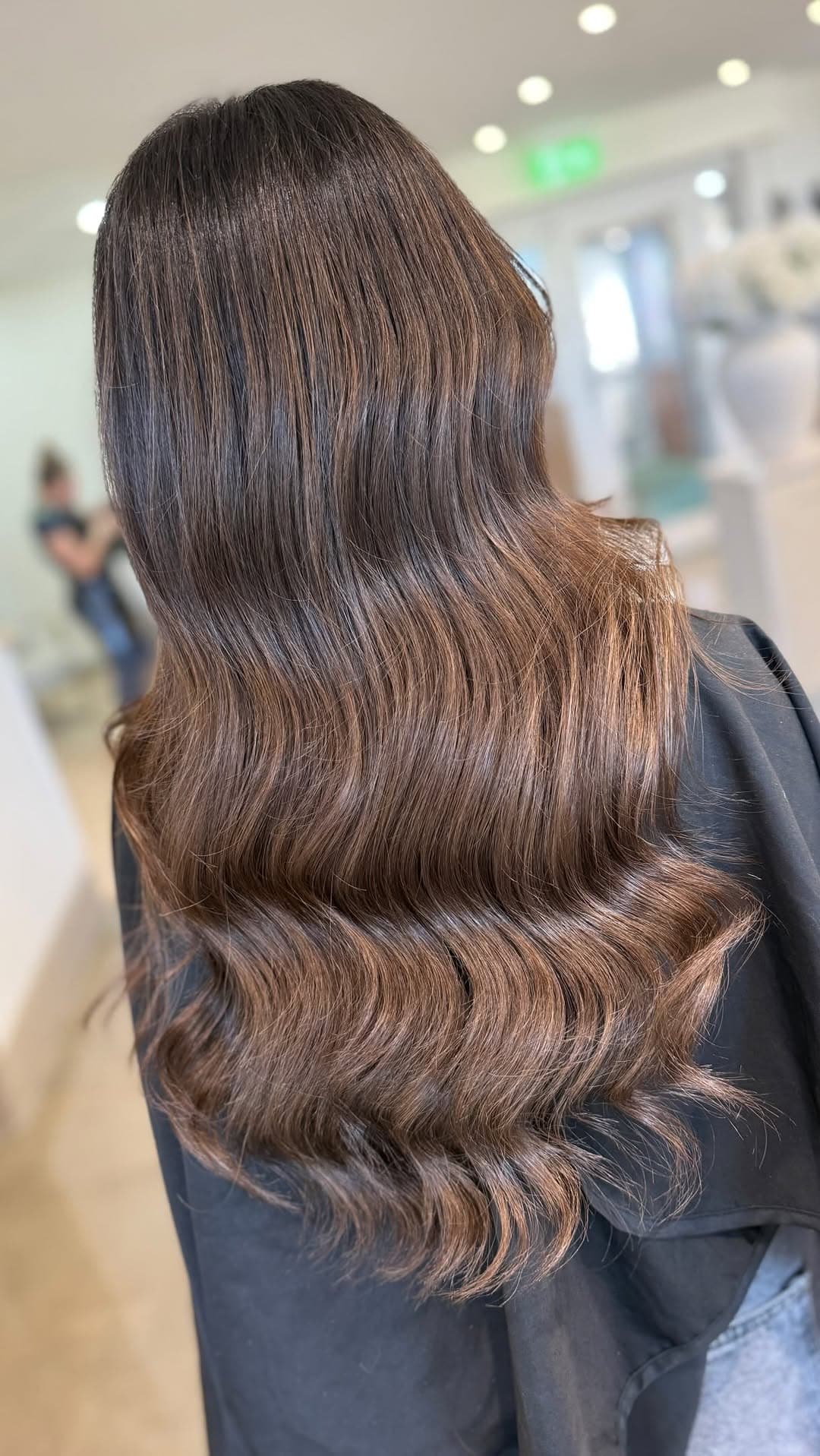 A glossy espresso, dark-brunette waved cascade on the salon's black gown — the root of the colour melt.