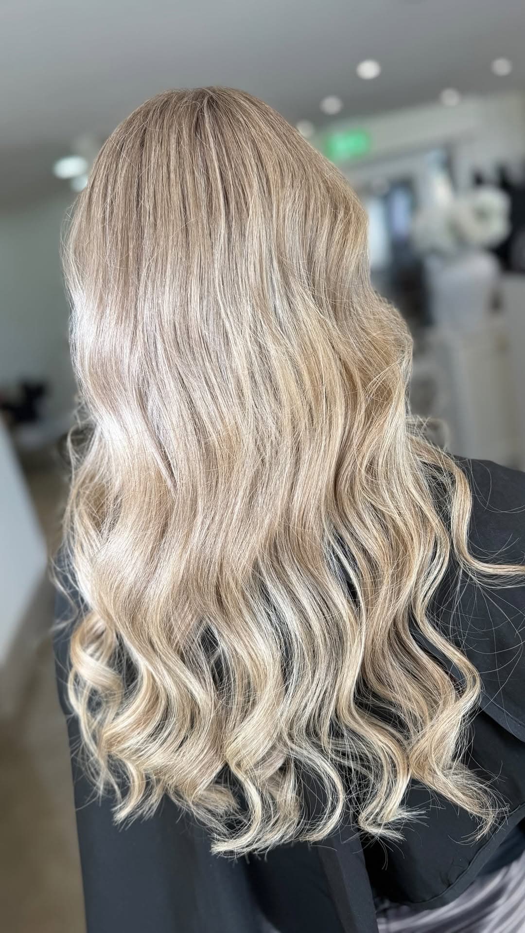 A luminous, lived-in blonde waved cascade in the bright salon interior.